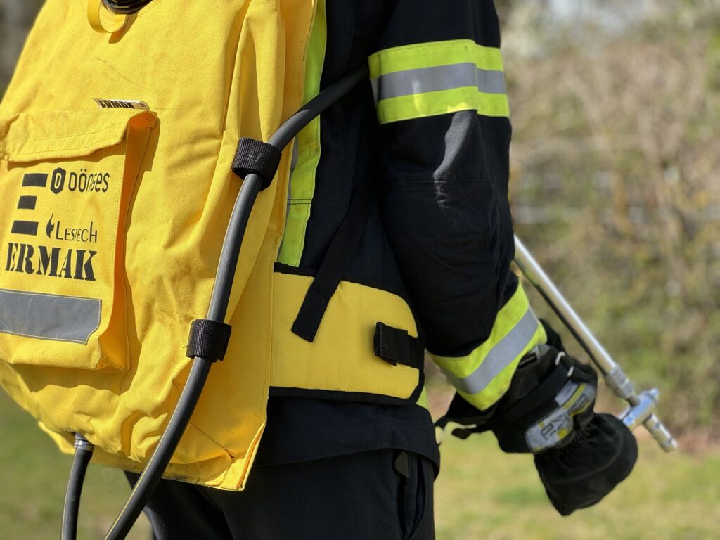 Foto von einer Feuerwehrkraft, die einen Löschrucksack auf dem Rücken und die Lanze in der Hand hat.